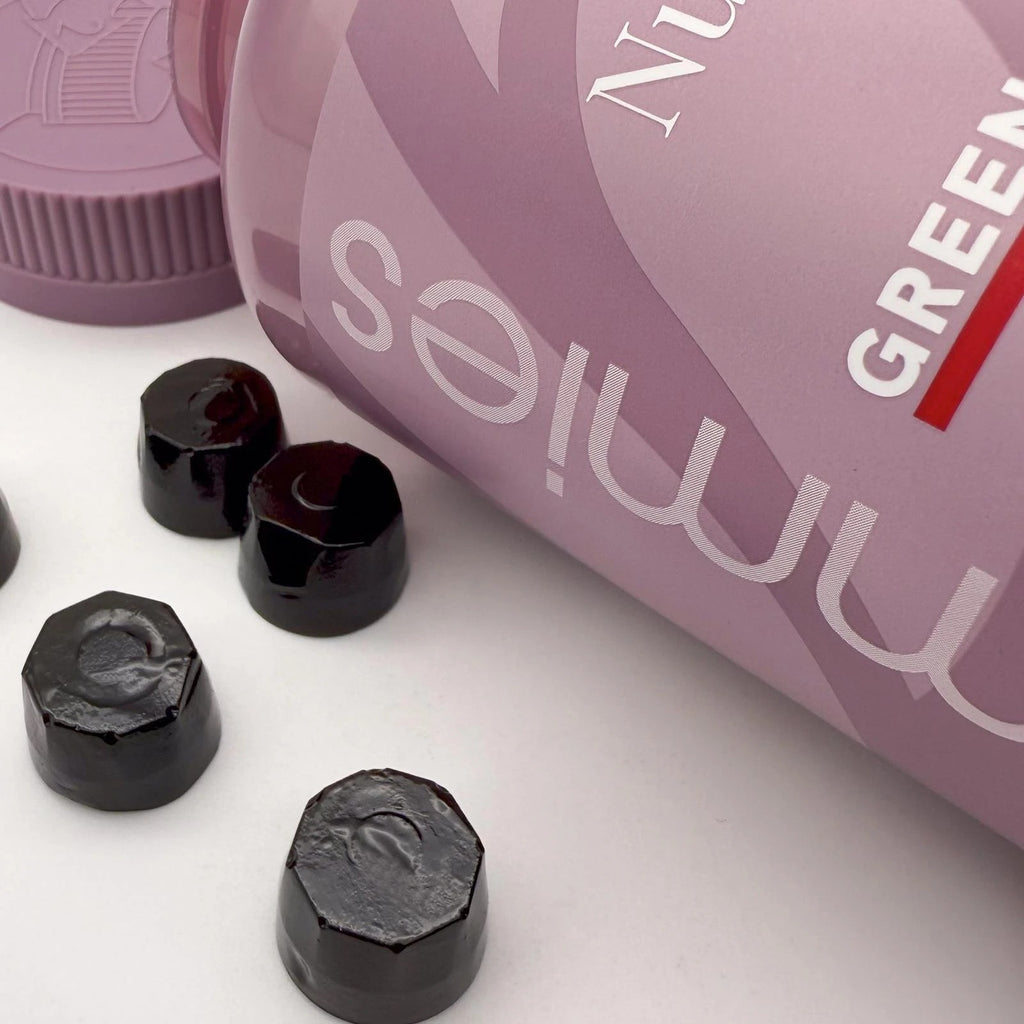 Black hexagonal gummy bears with a pink container labeled 'Green Gummies' on a white surface.