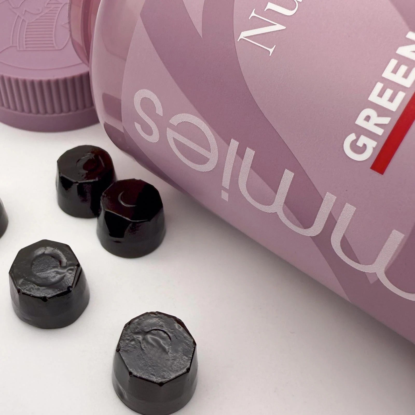 Black hexagonal gummy bears with a pink container labeled 'Green Gummies' on a white surface.